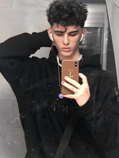 a young man taking a selfie in the mirror with his cell phone while wearing ear buds