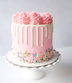 a pink frosted cake with sprinkles and icing on a plate