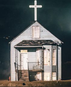 a small white church with a cross on it's roof and stairs leading up to the door