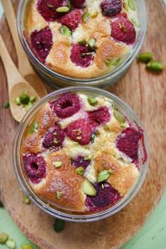 two desserts with raspberries and pistachio toppings on a wooden board