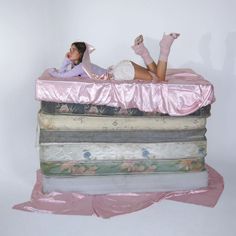 a woman laying on top of a stack of mattresses with pink satin coverings