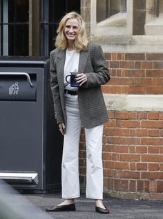 a woman standing next to a brick building holding a cup in her hand and smiling