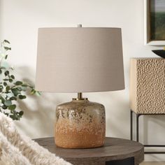 a table lamp sitting on top of a wooden table next to a white rug and potted plant