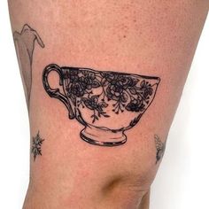 a black and white tattoo of a teacup with flowers on it's side