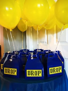 yellow balloons are in the air above blue jugs with drop on them, sitting on a table