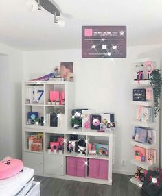 a room with white shelves and pink bins on the wall next to a bed