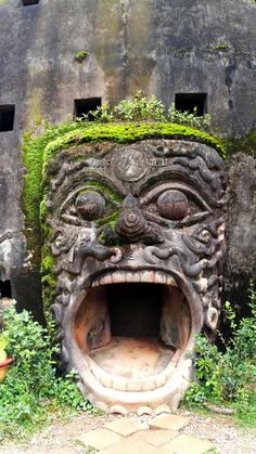 a stone face with moss growing on it's side in front of a building