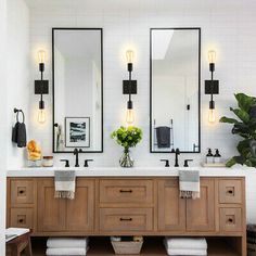 a bathroom with two sinks and mirrors on the wall next to a plant in a vase