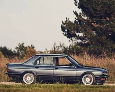 a black car parked on the side of a road next to tall grass and trees