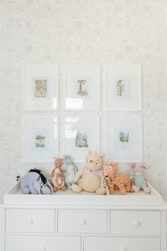 a white dresser topped with stuffed animals next to framed pictures on the wall above it