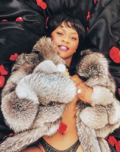 a woman laying on top of a bed wearing a fur coat with red hearts all over it