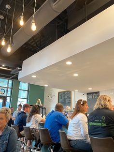 people sitting at tables in a restaurant with food on the table and hanging lights above them