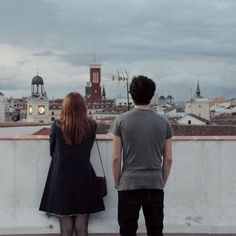 two people standing on top of a roof looking at the city