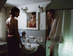 a man and woman standing in front of a bathroom mirror looking at each other's reflection