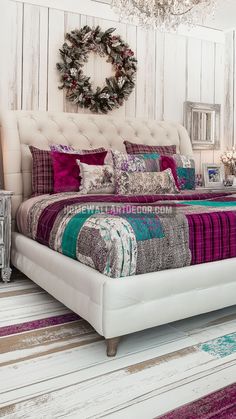 a white bed with purple and green comforter in a room next to a chandelier