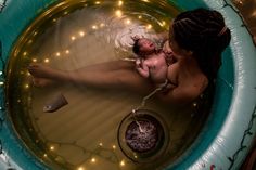 a woman holding a baby in a tub with lights on the wall behind her and water running through it