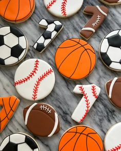 decorated cookies with sports themed icing on a marble countertop, including basketballs and soccer balls