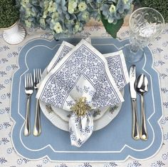 a place setting with blue and white napkins, silverware and flowers in the background