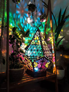 a multicolored lamp sitting on top of a wooden shelf next to potted plants