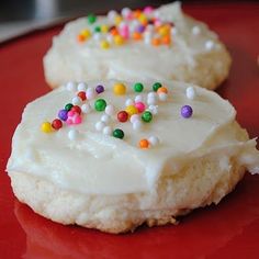 two cookies with white frosting and sprinkles on a red tablecloth