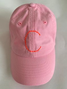 a pink baseball cap with an orange c embroidered on the front and side, sitting on a white surface