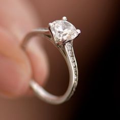 a close up of a person's hand holding a ring with a diamond on it