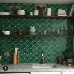 a kitchen with green tiles and shelves filled with dishes, cups, bowls and utensils