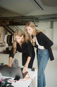 two young women looking at a laptop computer in front of a desk with other items on it