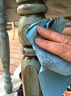 a hand holding a blue cloth on top of a wooden table next to a chair