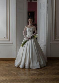 a woman in a white wedding dress standing on a hard wood floor with her hands on her hips