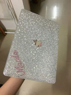 an apple laptop covered in silver sequins on a tiled floor with someone's hand holding it