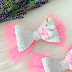 two pink and white hair bows with unicorns on them sitting next to purple flowers