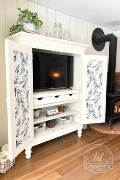 a white entertainment center with a television on it's stand in front of a wood burning stove