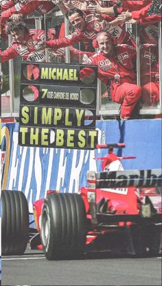 a red race car driving past a large group of people in front of a sign