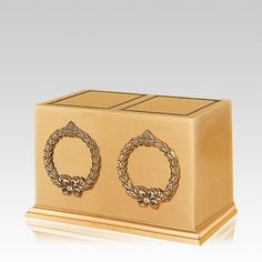 a golden box with two gold rings on the front and one in the middle, sitting on a white surface