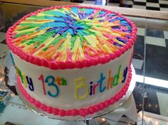 a birthday cake with colorful frosting on a glass table in a store display case