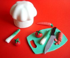 a knife, carrots and tomatoes on a green cutting board next to a white chef's hat