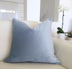 a blue pillow sitting on top of a white couch next to a vase with flowers