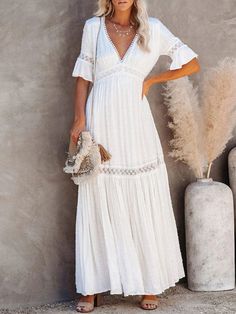 a woman wearing a white dress standing next to a plant and holding a handbag