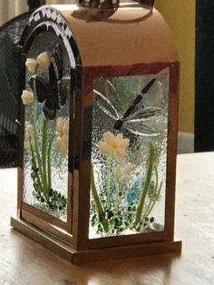 a glass block with flowers and dragonflys on the top is sitting on a table