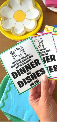 someone is holding up some dinner menus on a table with plates and napkins