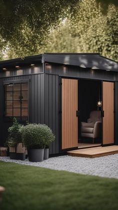 a small black shed sitting in the middle of a lush green yard with potted plants