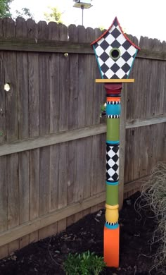 a colorful birdhouse sitting on top of a wooden pole next to a garden area