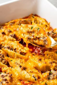 a casserole dish with meat and cheese being scooped from the casserole