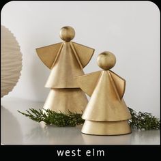 two gold christmas tree ornaments sitting on top of a white table next to a vase