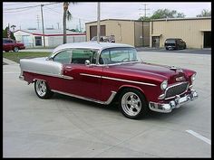 an old red and silver car parked in a parking lot next to a garage building