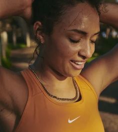 a woman in an orange tank top is holding her hands behind her head and smiling