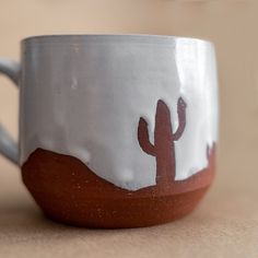 a white and brown coffee cup with a cactus design on the side, sitting on a table