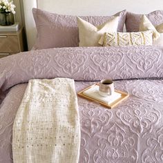 a bed with purple comforter and pillows on it, next to a tray full of flowers