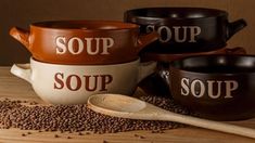 four soup bowls with spoons sitting on top of a wooden table next to brown beans